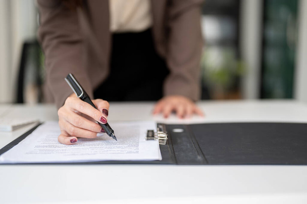 Γκρο πλαν εικόνα μιας επιχειρηματία που διαβάζει έγγραφα ή ένα συμβόλαιο, υπογράφοντας την υπογραφή της σε μια σύμβαση στο γραφείο της. - Φωτογραφία, εικόνα