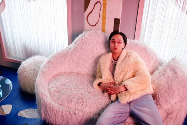 Kürk ve parti kıyafeti giymiş Asyalı bir gencin portresi. Pembe neon ışıklarla aydınlatılmış dinlenme odasında dinleniyor. - Fotoğraf, Görsel