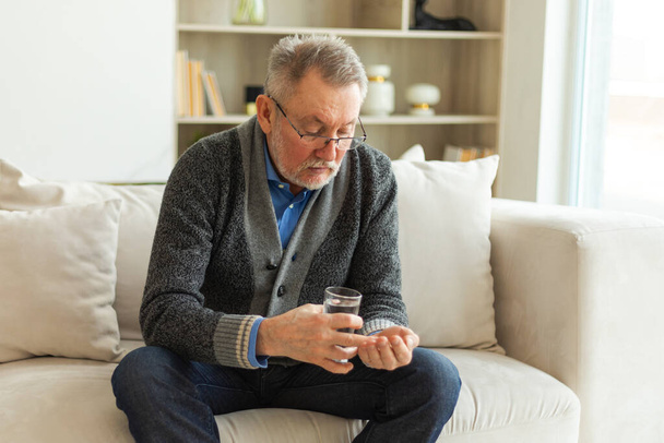 Middle aged senior man holding medical pill and glass of water. Mature old senior grandfather taking medication cure pills vitamin. Age prescription medicine healthcare therapy concept - Photo, Image