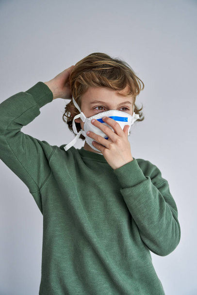 Enfant en vêtements décontractés portant un respirateur médical pendant les mesures restrictives de verrouillage et faisant face à une nouvelle normale - Photo, image