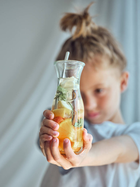 さまざまな柑橘類の果物およびスパイスから成っているおいしいレモネードのガラスを示す子供の柔らかい焦点 - 写真・画像