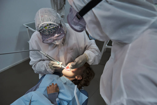 Сверху стоматолог и ассистент в форме обследования зубов пациента при работе с зубными инструментами в современной клинике - Фото, изображение