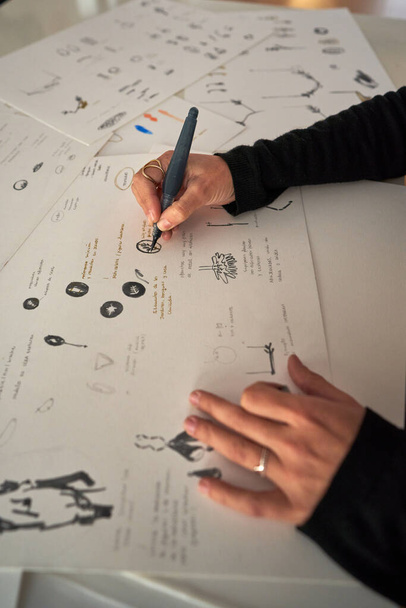 Υψηλή γωνία της καλλιέργειας ανώνυμη ταλαντούχα γυναίκα σχεδιαστής σκίτσο του διάφορα εξαρτήματα σε χαρτί σε εργαστήριο κοσμημάτων - Φωτογραφία, εικόνα