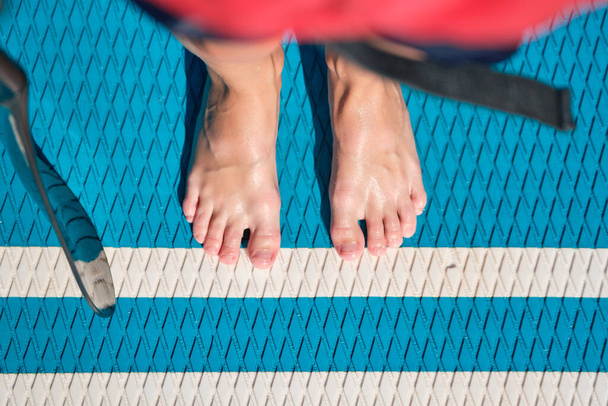 Blick von oben auf eine unkenntliche Person, die einen gesunden Lebensstil führt und am Sommerwochenende Schwimmen auf dem Paddelbrett übt - Foto, Bild