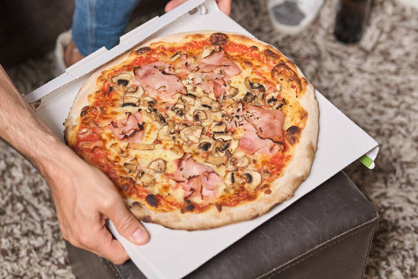 De dessus de la boîte de carton d'exploitation masculine anonyme de récolte avec pizza pour aller avec des champignons et du jambon à la maison - Photo, image