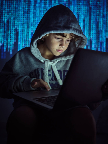 Crop kid hacker dactylographier sur ordinateur portable tout en rendant la cybercriminalité floue fond de code binaire dans la lumière tamisée - Photo, image
