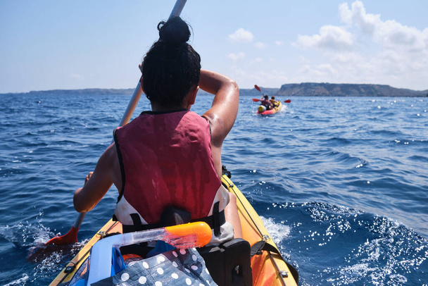 トロピカルリゾートでの夏の旅行中に熟した海に浮かんでいる間,パドルでカヤックを漕ぐ認識できない女性の旅行者のバックビュー - 写真・画像