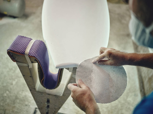 Planche de surf de polissage artisanale masculine méconnaissable d'en haut avec un tissu spécial abrasif en atelier - Photo, image
