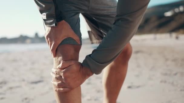 Knee pain, beach and legs of sports runner with health risk, exercise wound and emergency outdoor. Fitness man, ocean and closeup on hands of athlete with joint injury, first aid and workout accident. - Кадры, видео