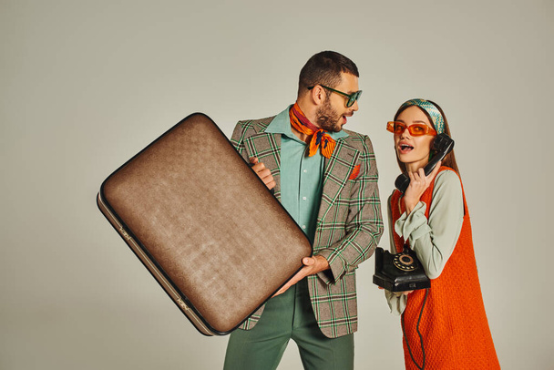 homme excité avec valise vintage près de femme de style rétro parlant sur téléphone à fil sur gris - Photo, image