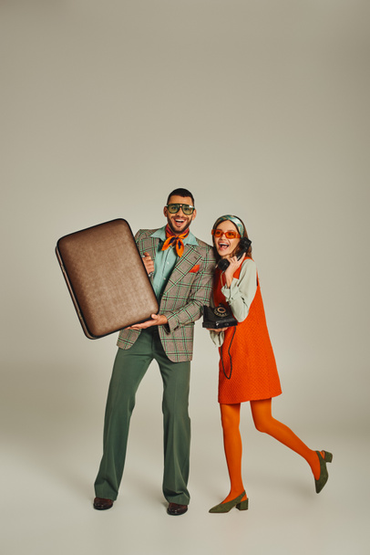 homme joyeux avec valise vintage près de la femme parlant sur téléphone rétro sur gris, couple à l'ancienne - Photo, image