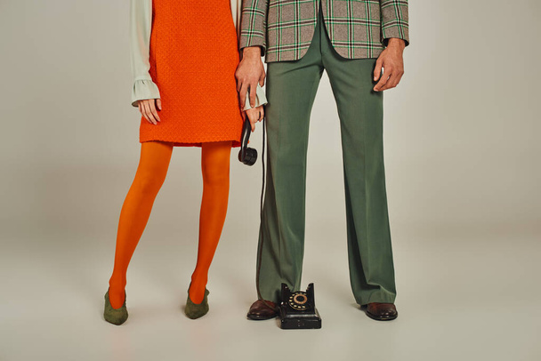 oříznutý pohled na pár v módním retro oblečení stojící s sluchátkem z retro telefonu na šedé - Fotografie, Obrázek