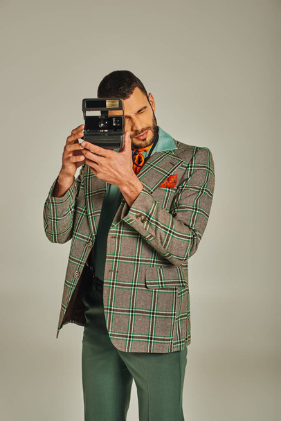 stylish man in checkered jacket taking photo on vintage camera on grey, old-fashioned style - Photo, Image