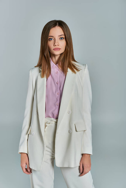junge stilvolle Frau im weißen eleganten Anzug mit Blick in die Kamera auf graue, klassisch minimalistische Mode - Foto, Bild