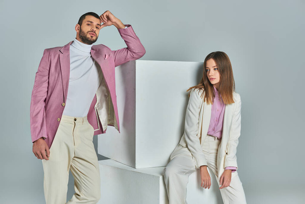 trendy man in lilac blazer looking at camera near white cubes and stylish woman sitting on grey - Photo, Image