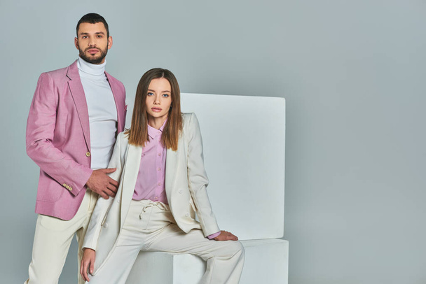 woman in white suit and man in lilac blazer looking at camera near white cubes on grey, trendy wear - Photo, Image