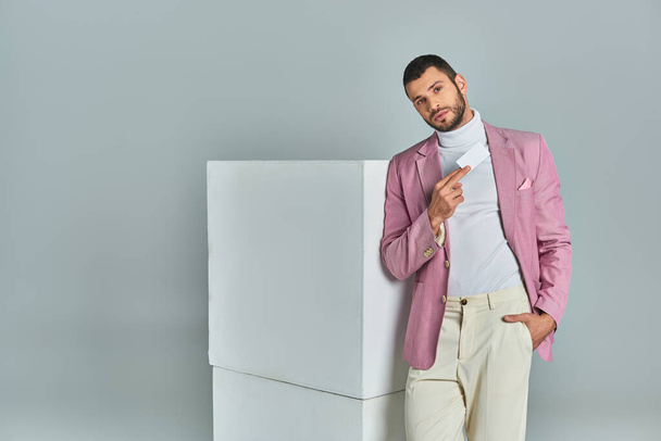 homem na moda em blazer lilás posando com a mão no bolso e cartão de visita em branco perto de cubos em cinza - Foto, Imagem