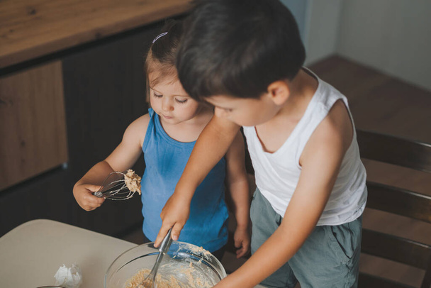 Χαριτωμένα παιδιά χτυπώντας υλικά στο μπολ ενώ ψήνονται στην κουζίνα. Οικογενειακές συνταγές για διακοπές. - Φωτογραφία, εικόνα