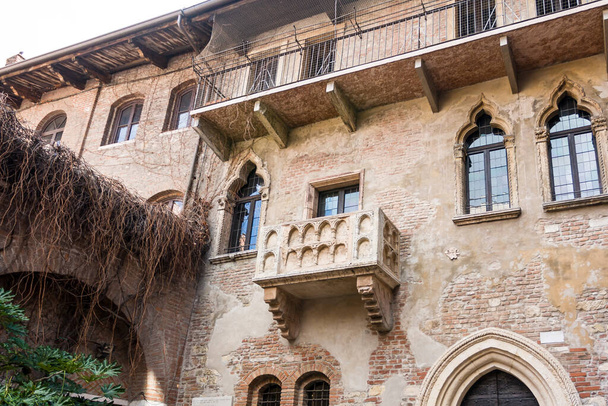 Buitengevel van een oud verweerd palazzo in Verona, Italië met sierlijke gotische ramen en balkon - Foto, afbeelding