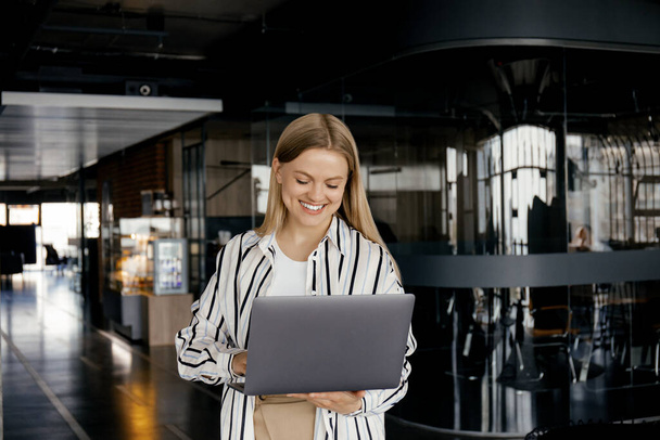 Ein attraktives junges Mädchen arbeitet im Büro an einem Laptop - Foto, Bild
