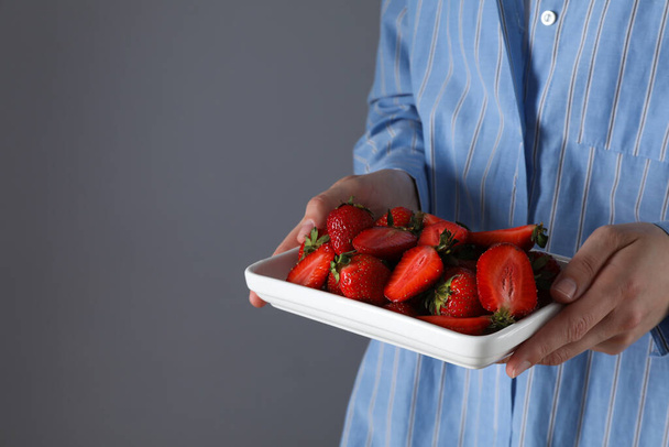 Strawberries on plate in female hands on gray background, space for text - Фото, зображення