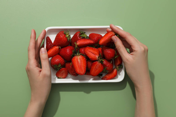 Strawberries on plate and female hands on green background, top view - Foto, afbeelding