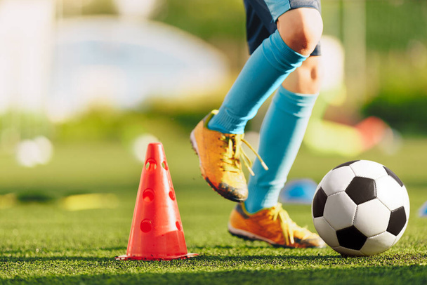 Egy focista lábai kék zokniban és stoplikban futnak és csöpögnek a labdával. Foci edzésen lévő gyerekek. Focista futtatja a labdát edzés közben. Sportcsarnok a háttérben - Fotó, kép