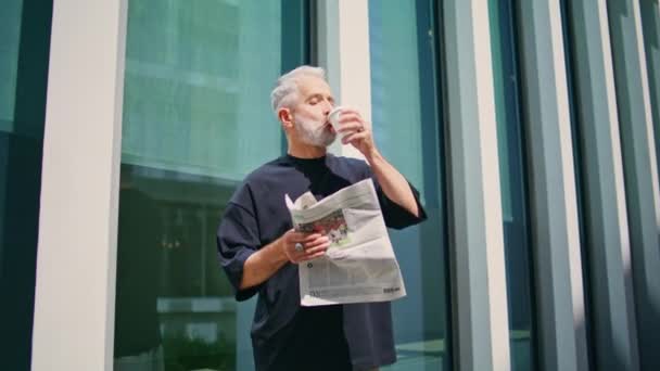 Starý obchodník pije kávu v centru. Pozorný senior si četl noviny a užíval si ranní rutiny na městské ulici. Zaostřené šedé vlasy muž výkonný odpočinek v současné kancelářské budově. - Záběry, video