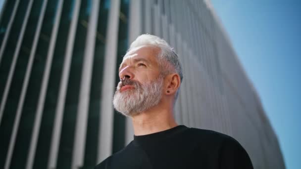 Bearded man posing urban building closeup. Confident senior male wear piercing looking camera at city downtown. Successful old businessman investor resting on sunny street alone. Brutal rock musician - Footage, Video