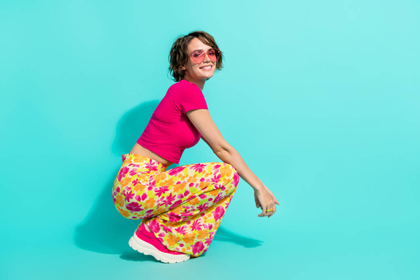Full length photo of cool funky lady flower print pants sitting empty space isolated turquoise color background. - Фото, зображення