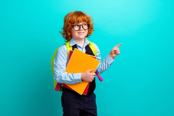 Portrait of little intelligent schoolkid hold notebook carry rucksack look direct finger empty space isolated on turquoise color background. - Φωτογραφία, εικόνα