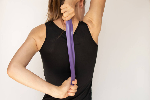 The girl is engaged in fitness with a fitness rubber band on a white background, hands and posture with a fitness rubber band, trains - Photo, Image