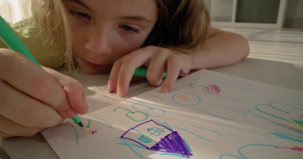 Un enfant dessine une maison avec des crayons sur papier. Une fille heureuse est couverte d'art, le concept de la chaleur de la maison et de la famille. Images 4k de haute qualité - Séquence, vidéo