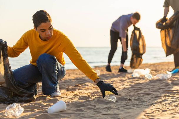 Giornata della Terra. Gli attivisti volontari raccolgono la pulizia della spazzatura della zona costiera della spiaggia. Donna e uomo mettono la spazzatura di plastica nel sacco della spazzatura sulla riva dell'oceano. Pulizia delle zone costiere di conservazione ambientale - Foto, immagini