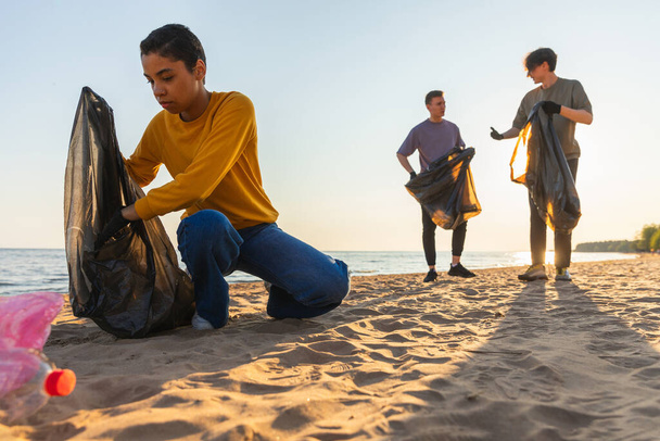 Dia da Terra. Ativistas voluntários recolhem limpeza de lixo da zona costeira da praia. A mulher e o homem põem lixo plástico no saco do lixo na costa oceânica. Conservação do ambiente limpeza da zona costeira - Foto, Imagem