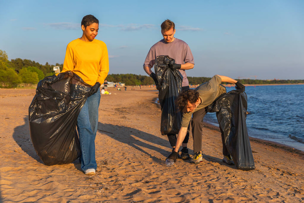 Ημέρα της Γης. Εθελοντές ακτιβιστές συλλέγουν σκουπίδια καθαρισμού της παράκτιας ζώνης. Γυναίκα με σκουπίδια σε σακούλα σκουπιδιών στην ακτή του ωκεανού. Καθαρισμός παράκτιων ζωνών προστασίας του περιβάλλοντος. Θολή εικόνα - Φωτογραφία, εικόνα