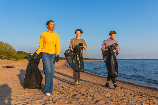 Dünya günü. Gönüllü eylemciler sahil bölgesindeki çöpleri topluyor. Okyanus kıyısında çöp torbası içinde kadın erkekler. Çevresel koruma kıyı bölgesi temizliği. Bulanık video - Fotoğraf, Görsel