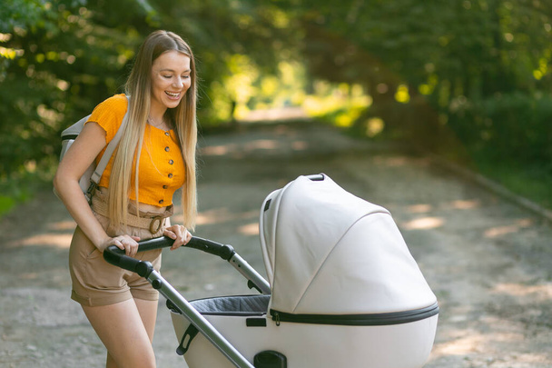 Vrolijke vrouw met rechte lange haar wandelingen met baby in trendy kinderwagen - Foto, afbeelding