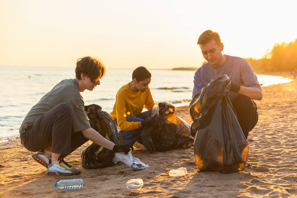 Dzień Ziemi. Zespół aktywistów wolontariuszy zbiera śmieci w strefie przybrzeżnej plaży. Grupa ludzi wkłada plastikowe śmieci do worków na śmieci na brzegu oceanu. Ochrona środowiska - Zdjęcie, obraz