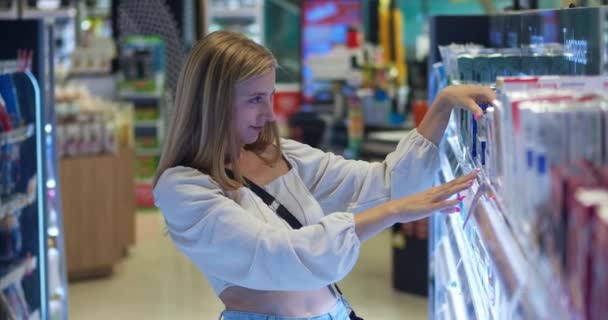 Kozmetik bölümünde bir süpermarkette çalışan bir kadın kendisine uygun bir ürün seçiyor, kendine dikkat ediyor. Kendine dikkat etme kavramı. Kadın süpermarkette raflardaki malları inceliyor.. - Video, Çekim