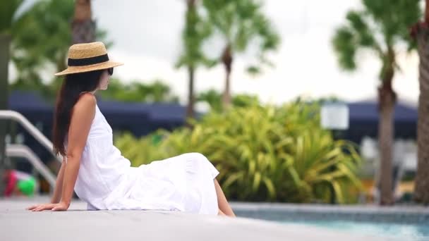 Zadní pohled na ženu v klobouku relaxační u venkovního bazénu v luxusním hotelovém resortu těší letní dovolenou - Záběry, video
