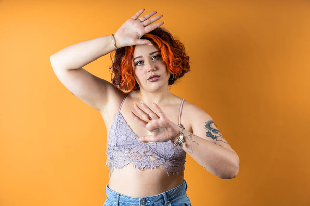 Modern tetovált nem bináris vörös hajú lány felemelt karokkal védelemben - Fotó, kép