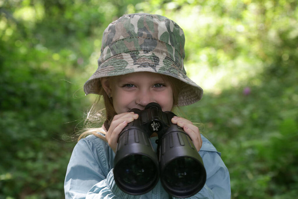 Linda niña explorando la naturaleza mirando a través de prismáticos. Niño jugando al aire libre. Los niños viajan, aventura y observación de aves concepto. - Foto, Imagen