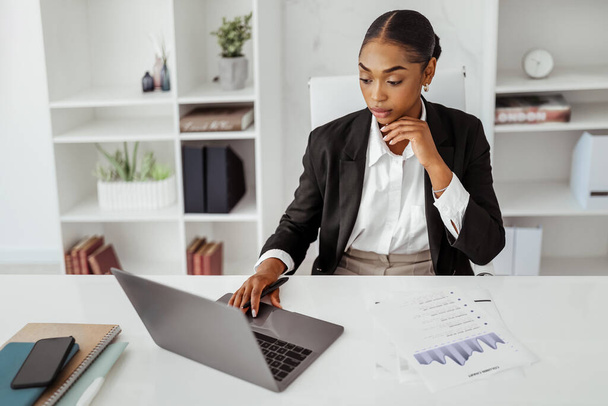 Fekete női vállalkozó dolgozik laptop és papírok a munkahelyen a modern irodában, üzletasszony formális viselet kezelése pénzügyi jelentések, másolás tér - Fotó, kép