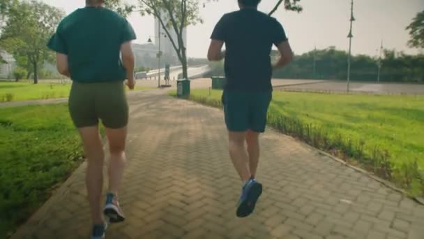 Вид сзади наклон вверх снимок спортивной пары в спортивной одежде, бегущей по тротуару в парке во время тренировки вместе на открытом воздухе утром - Кадры, видео