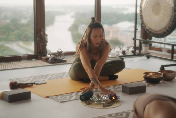 Una mujer en ropa deportiva practicando yoga en un entorno tranquilo dentro de un apartamento, con un paisaje urbano panorámico en el fondo - Foto, imagen