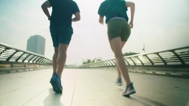 Back view low angle shot of athletic couple in sportswear running on footbridge in city while working out together outdoors in morning - Footage, Video