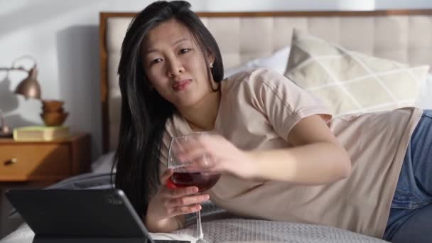 Ευτυχισμένη όμορφη γυναίκα με casual ρούχα που μιλάει σε βιντεοκλήση σε ψηφιακό tablet ξαπλωμένη στο κρεβάτι. Εργασία από το σπίτι online εκπαίδευση. Αναπαραγωγή online ψώνια παιχνίδι χαλάρωση. - Πλάνα, βίντεο