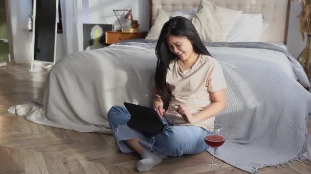 Boldog gyönyörű nő alkalmi ruhák dolgozik digitális tabletta ül az ágy mellett. Otthoni oktatás online koncepciója - Felvétel, videó