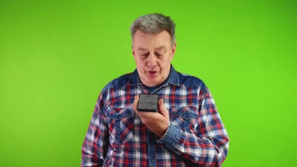 Ηλικιωμένος άνδρας κρατώντας smartphone και καταγράφει φωνητικό μήνυμα σε ανοιχτή ακρόαση. Χρήση έξυπνων τεχνολογιών για επικοινωνία μέσω μέσων κοινωνικής δικτύωσης, φωνητικές εντολές, μηνύματα. Πράσινη οθόνη, χρωματικό κλειδί. - Πλάνα, βίντεο